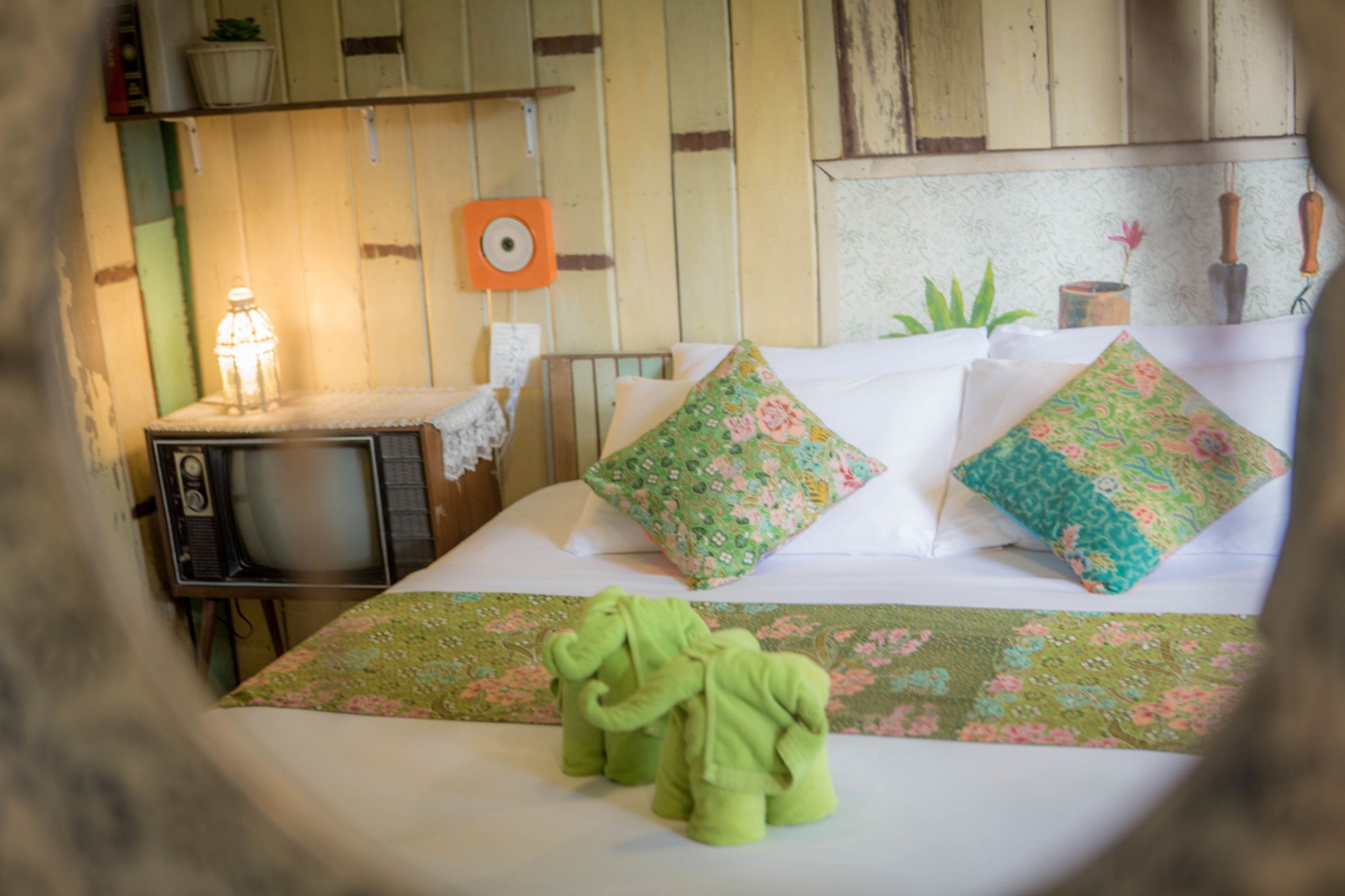 Un lit avec des coussins à motifs floraux, une couverture verte et deux serviettes vertes en forme d’éléphant.