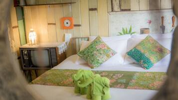 Un lit avec des coussins à motifs floraux, une couverture verte et deux serviettes vertes en forme d’éléphant.