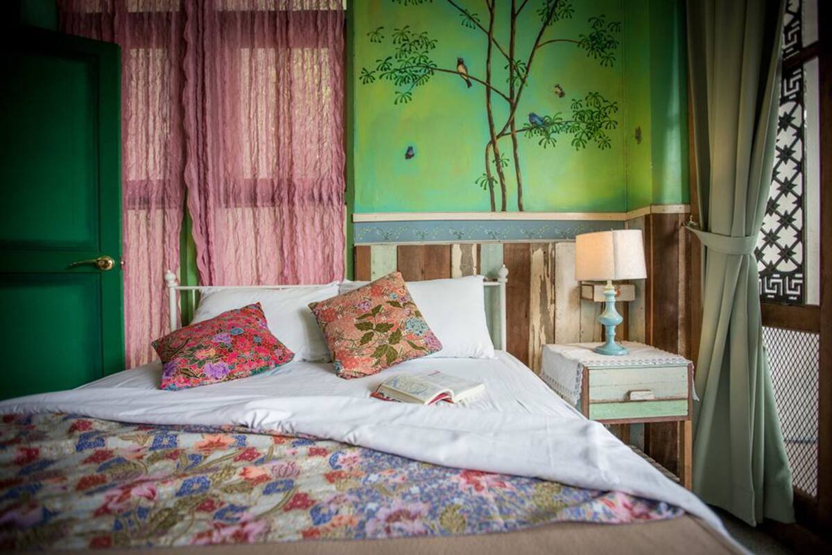 Un lit avec une literie à motifs floraux, deux oreillers, une table de chevet avec une lampe et une porte verte.