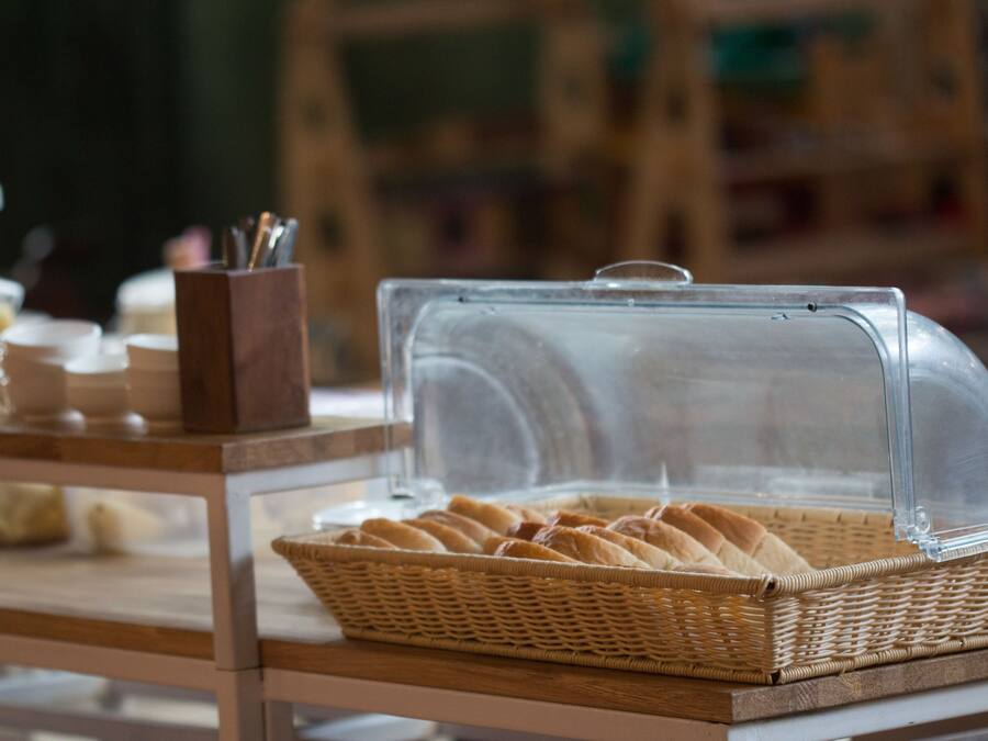 A breakfast buffet with a wicker basket of bread and a glass display case.