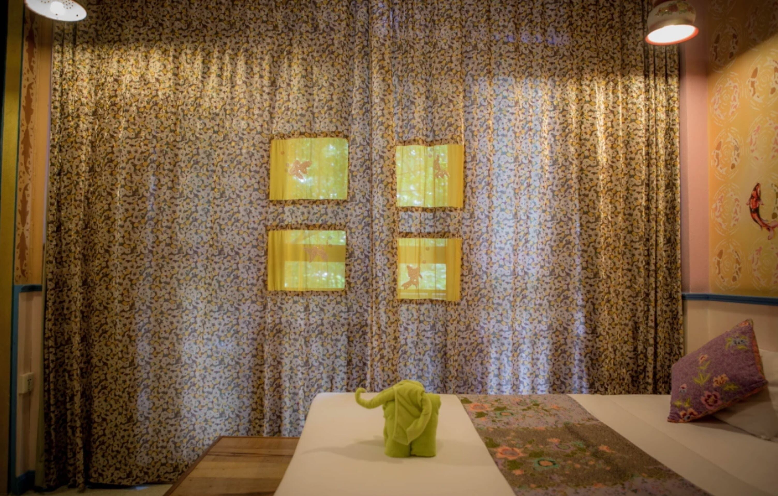 Una habitación con cortinas de estampado floral, una cama con un cojín en forma de elefante verde y una colcha estampada.