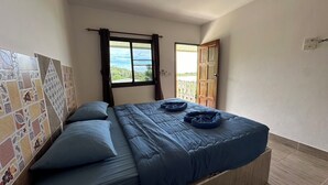 A bedroom with a bed, a view of the outdoors, and a tiled wall. - Cottage Hill at Lanta (Ko Lanta)