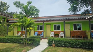 A two-story building with a green and yellow exterior, a covered outdoor seating area with plastic chairs, and a pathway leading to the entrance. - Cottage Hill at Lanta (Ko Lanta)