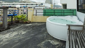 Een dak met een jacuzzi, potplanten en een uitzicht op gebouwen op de achtergrond.