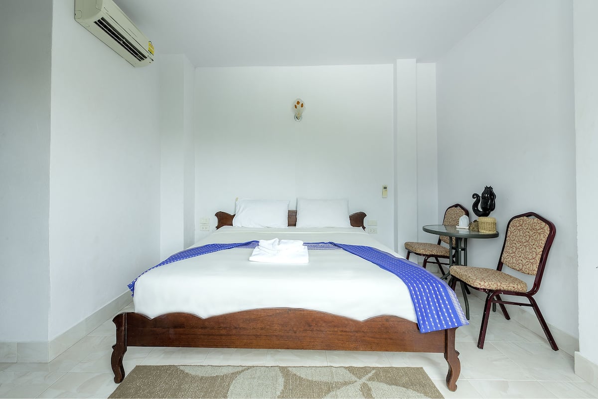 A neatly made bed with a white and blue bedspread, a wooden headboard, and a small table with chairs beside the bed.