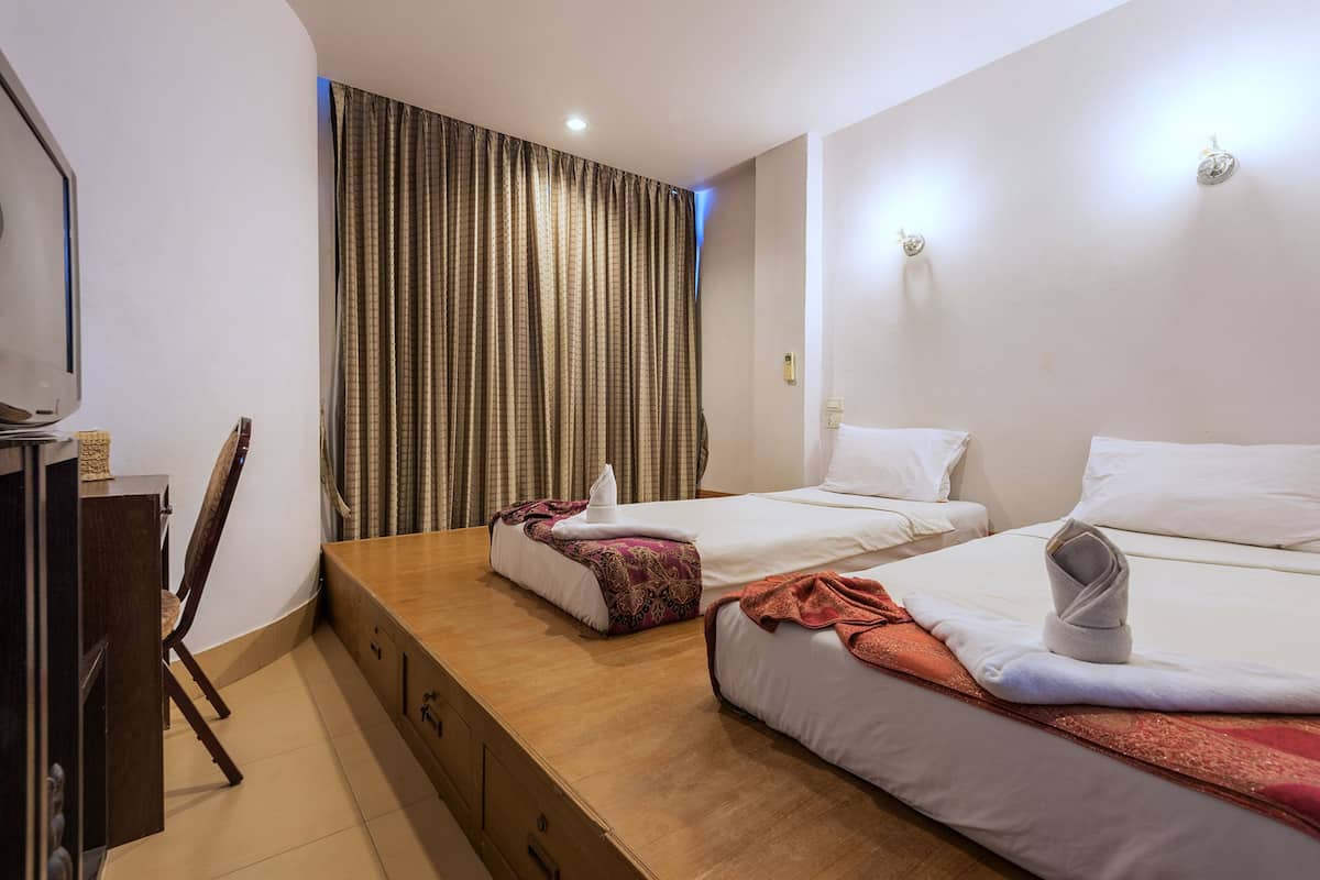 A hotel room with two beds, a wooden desk, a chair, and a large window with curtains.