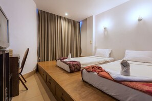 Een hotelkamer met twee bedden, een houten bureau, een stoel en een groot raam met gordijnen.