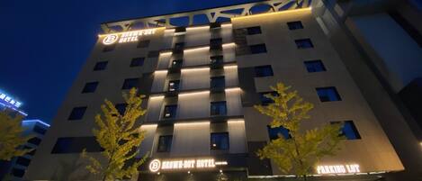 A multi-story hotel with a modern facade, illuminated signage, and a parking lot.
