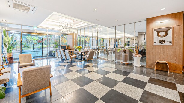 Un'ampia hall con pavimento a scacchi, zone relax e grandi finestre che offrono vista sull'esterno.