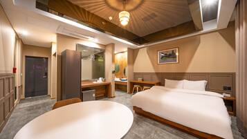 A hotel room with a large bed, a desk, a chair, a round table, a mirror, and a painting on the wall.