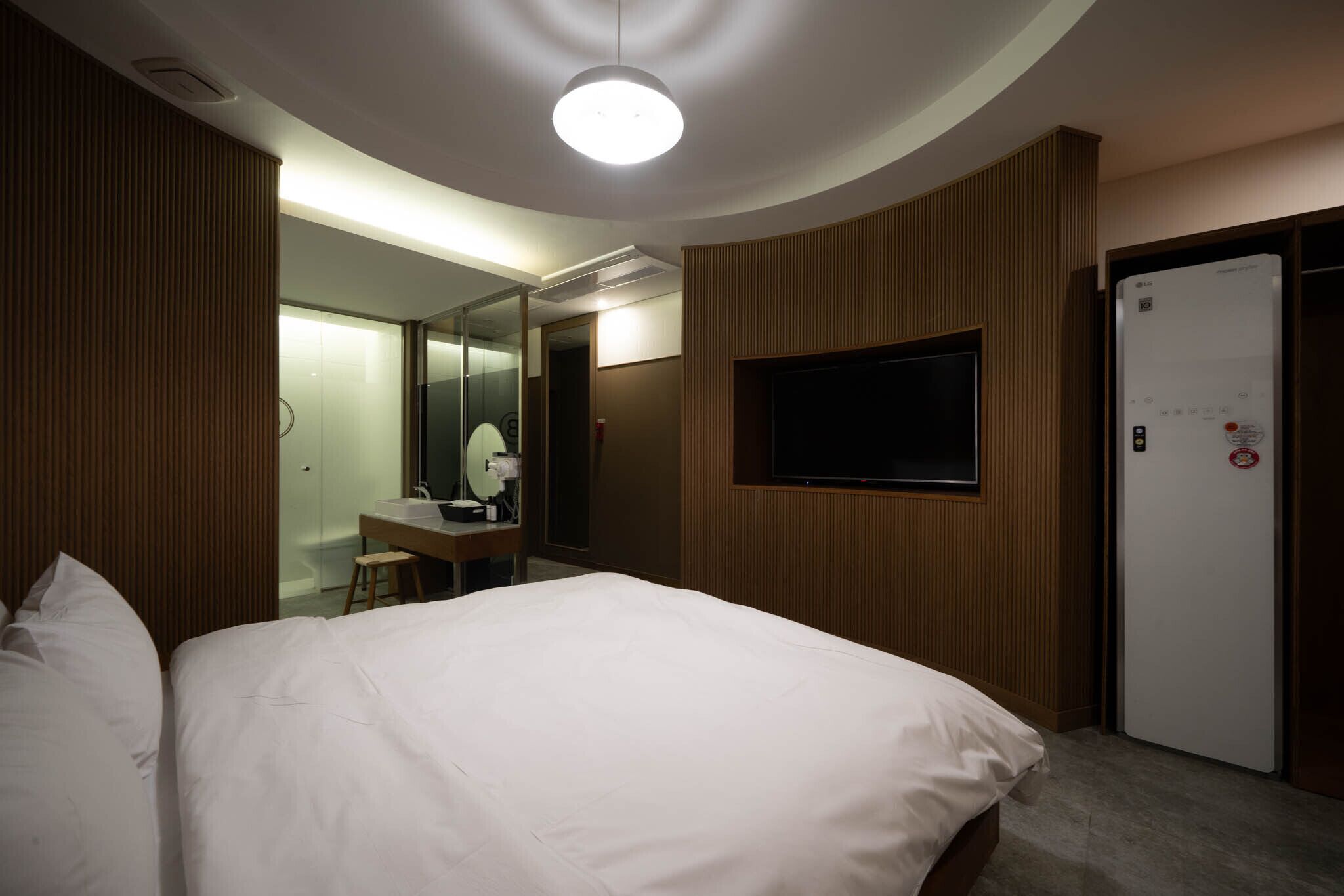 A hotel room with a large bed, a desk with a chair, a mirror, a television, and a door with a sign.