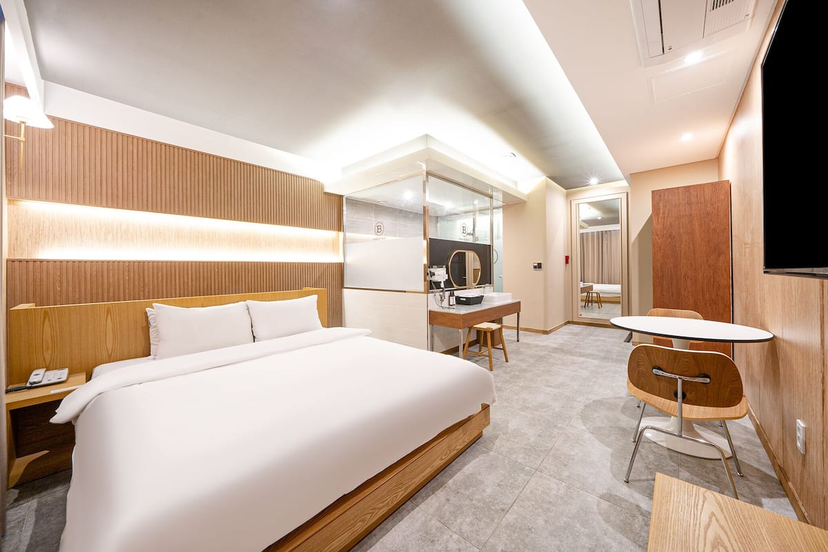 A modern hotel room with a large bed, a desk with a chair, a small table, and a TV.