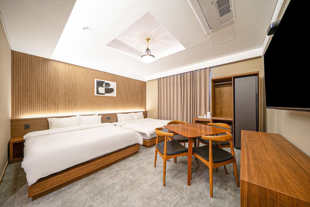 A hotel room with a large bed, a dining table with chairs, a ceiling light, and a television.