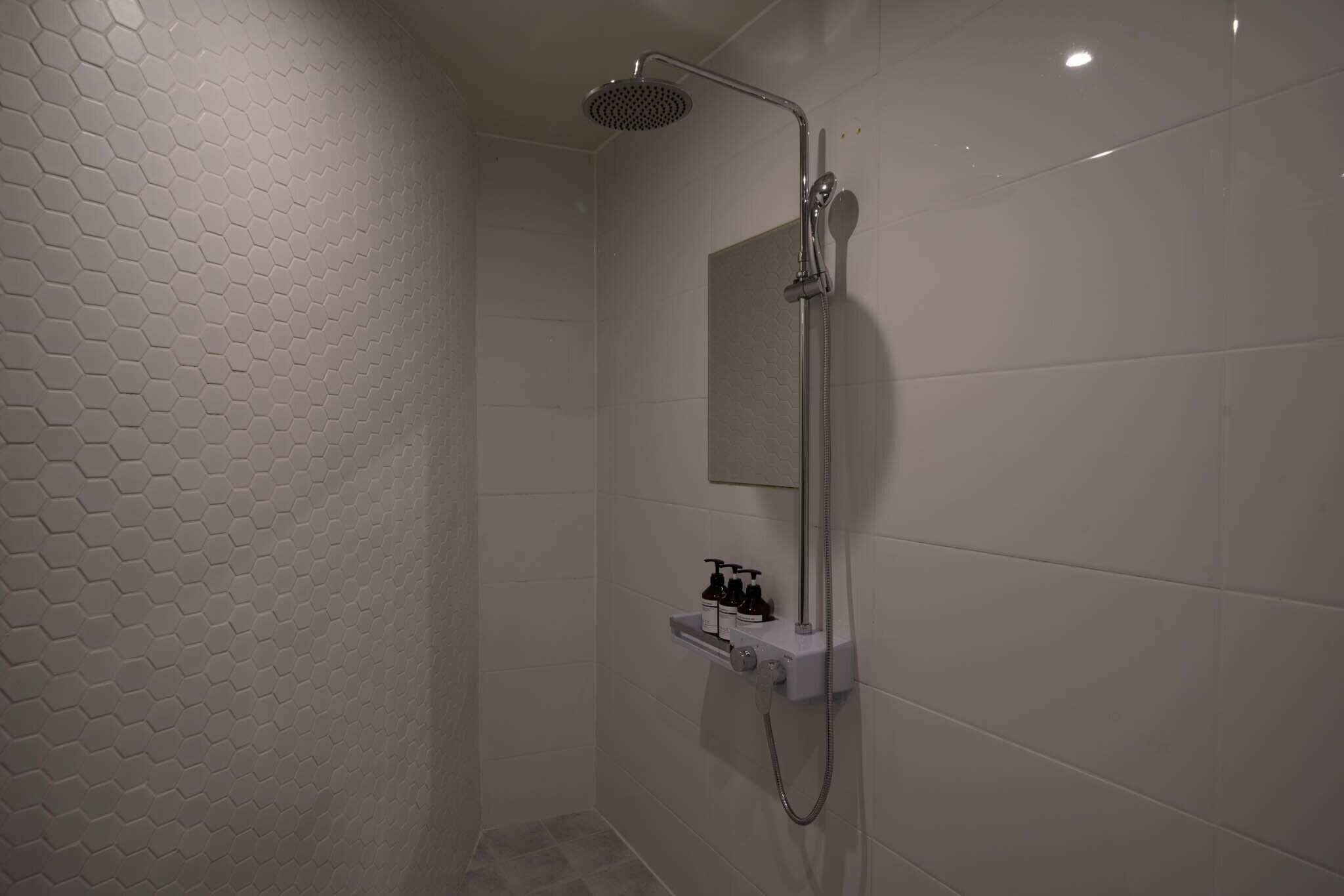 A modern shower with a handheld showerhead, a wall-mounted mirror, and a soap dispenser.