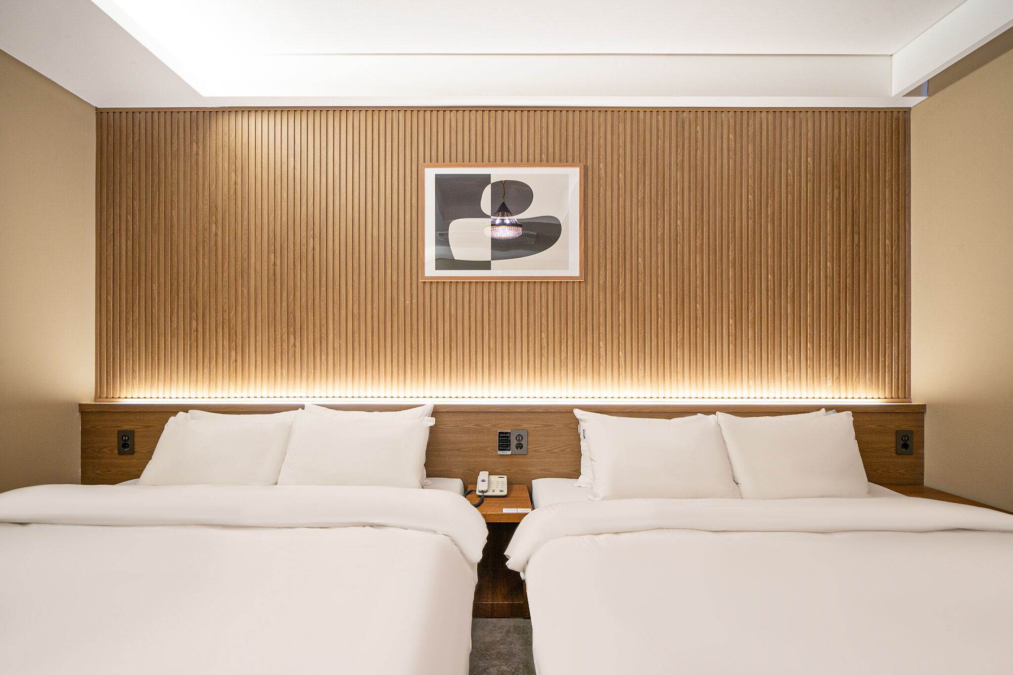 A hotel room with two beds, a wooden headboard, a framed artwork, and a bedside table with a phone.