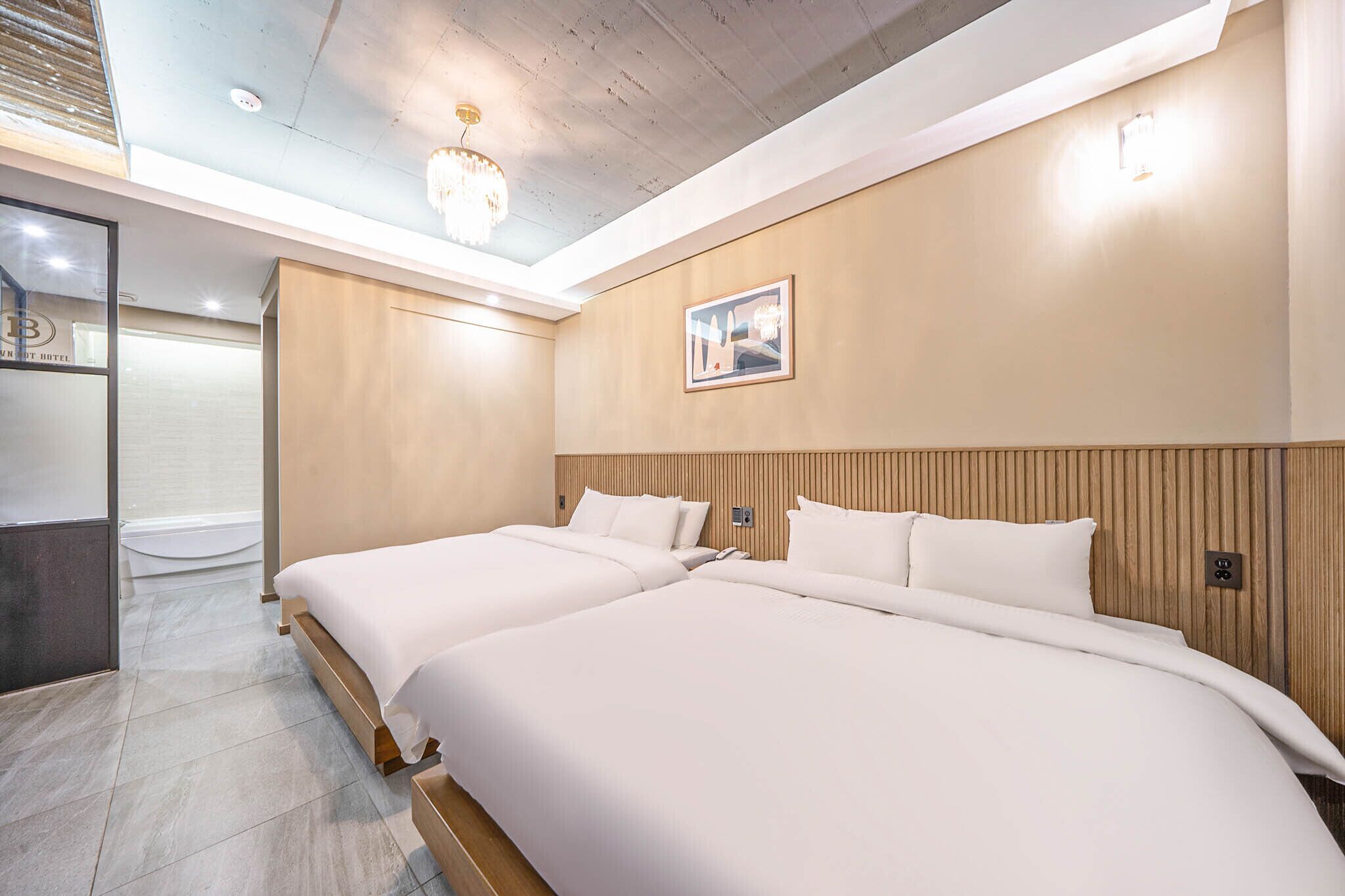 A hotel room with two beds, a wooden headboard, a ceiling light, and a framed picture on the wall.