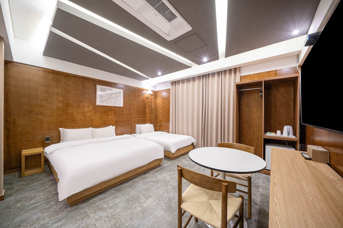 A hotel room with two beds, a dining table, a TV, and a wardrobe.