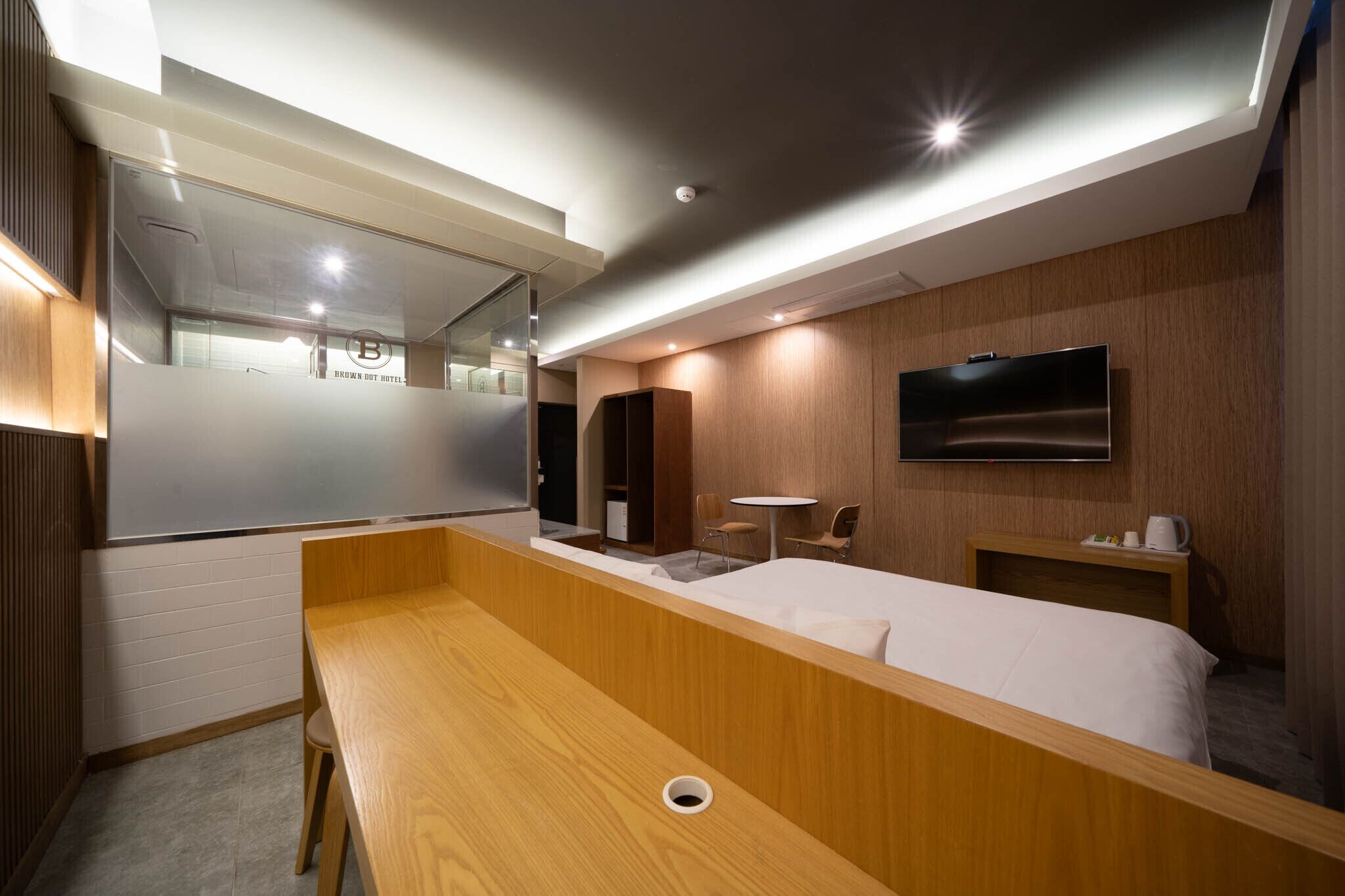 Una habitación de hotel moderna con una cama de madera, una mesita pequeña, un televisor montado en la pared y un espejo.