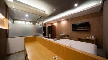 Una habitación de hotel moderna con una cama de madera, una mesita pequeña, un televisor montado en la pared y un espejo.