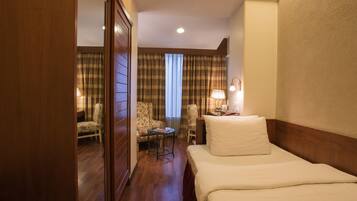A hotel room with a bed, a desk, a chair, a lamp, and a view of the hallway.