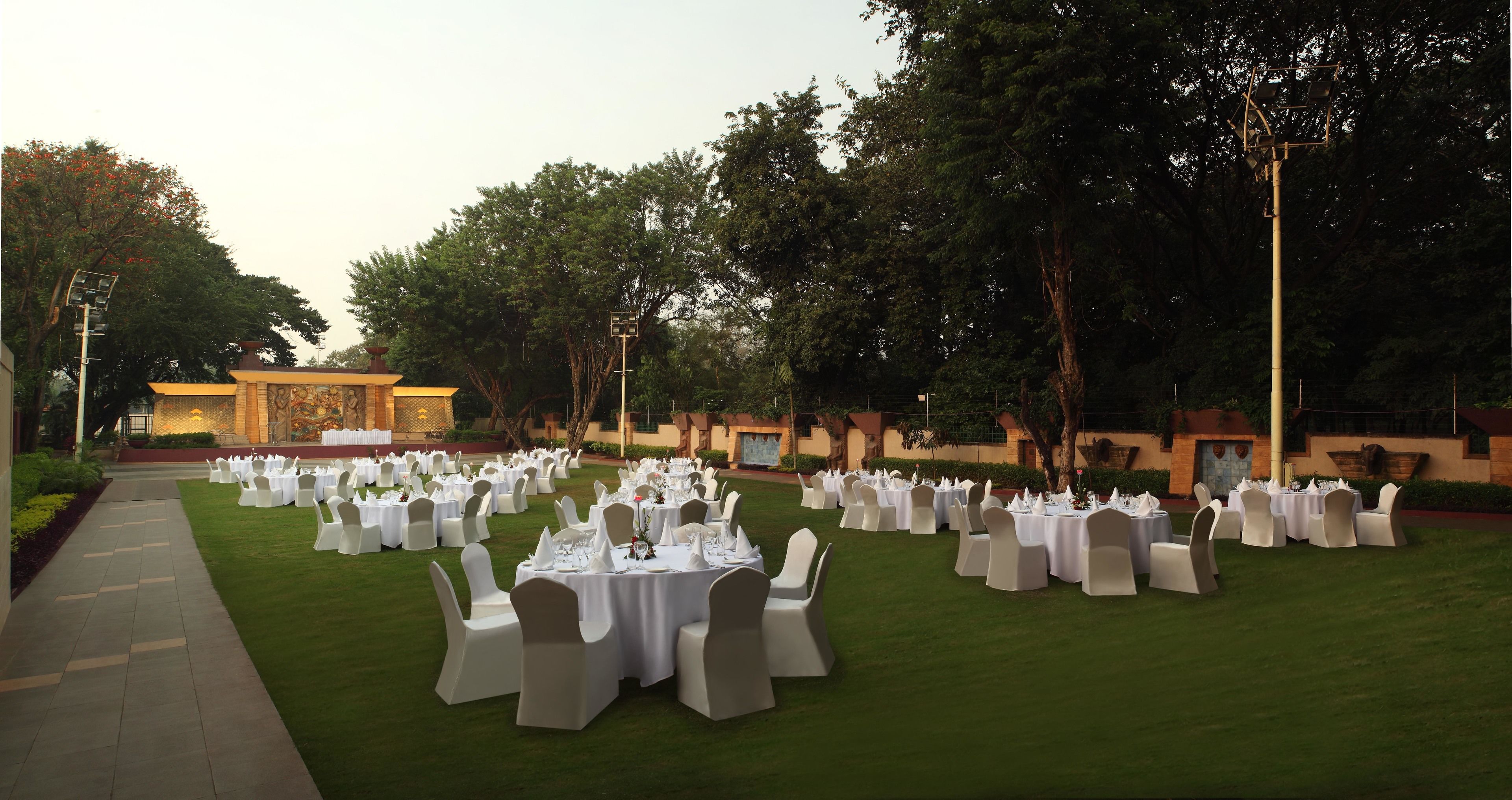 An outdoor event space with multiple round tables set up on a lawn, surrounded by white chairs.