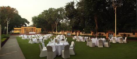 An outdoor event space with multiple round tables set up on a lawn, surrounded by white chairs.