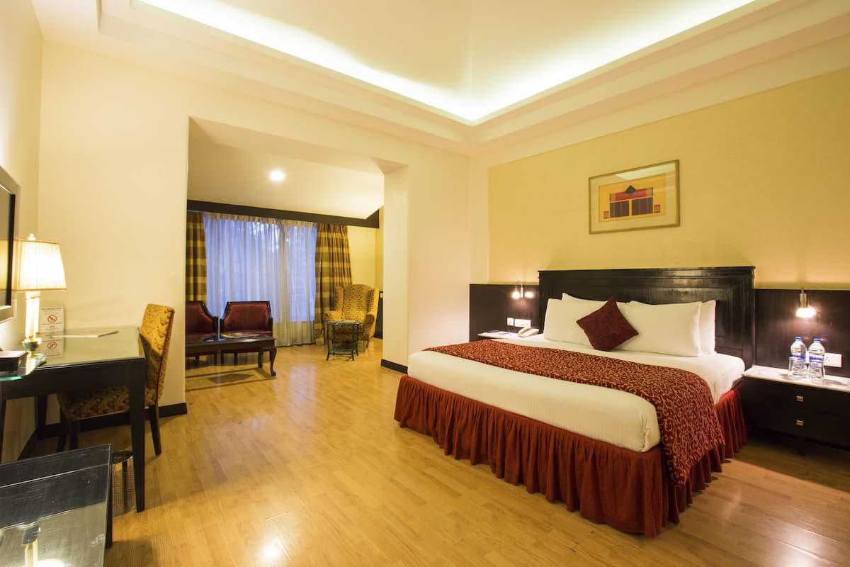A hotel room with a large bed, a desk with a lamp, a chair, and a dining table.