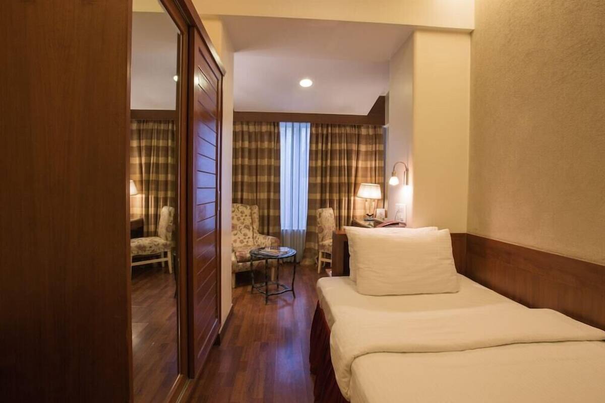 A hotel room with a bed, a desk, a chair, and a lamp.