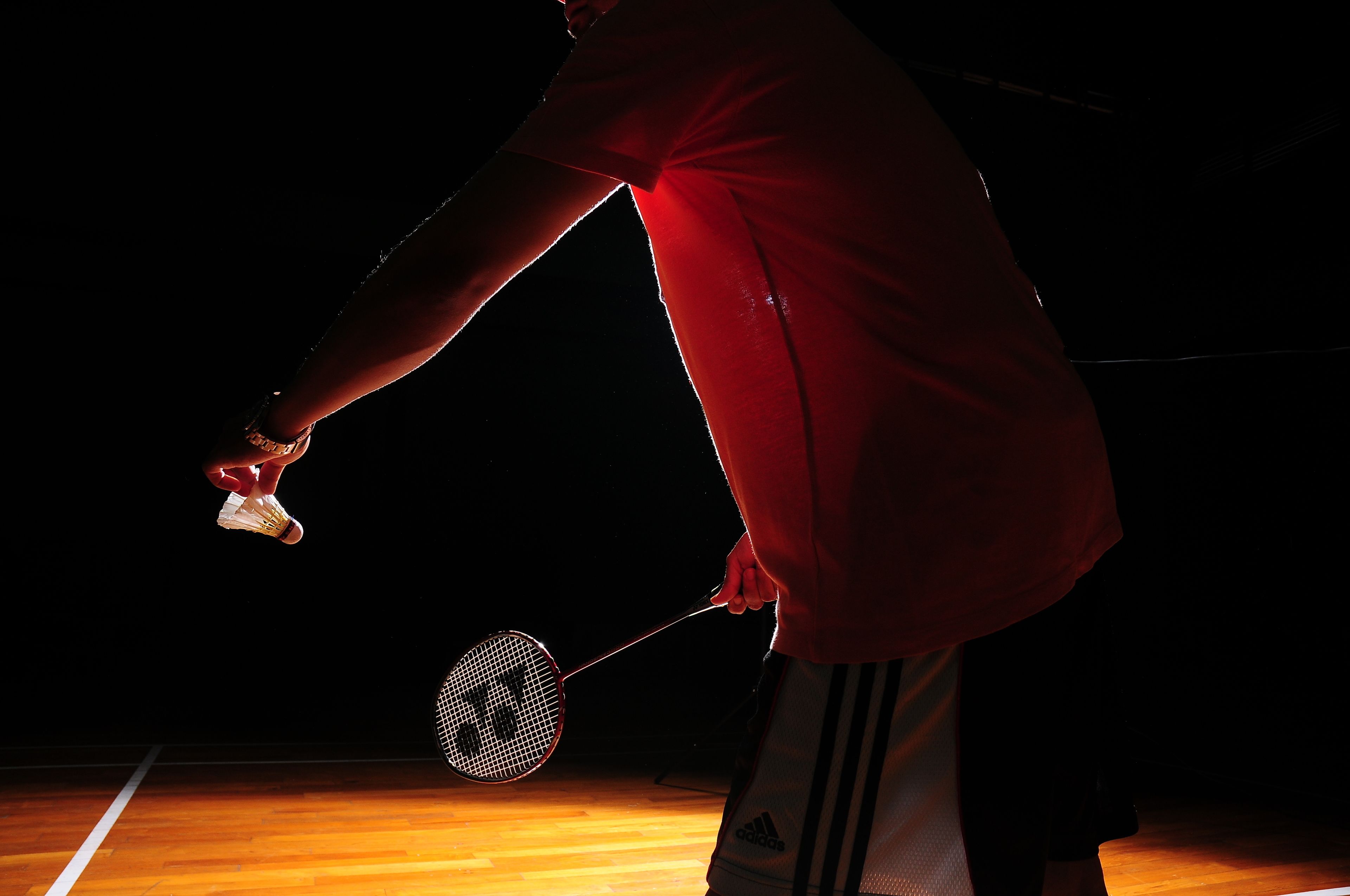 A person playing badminton on a wooden court.