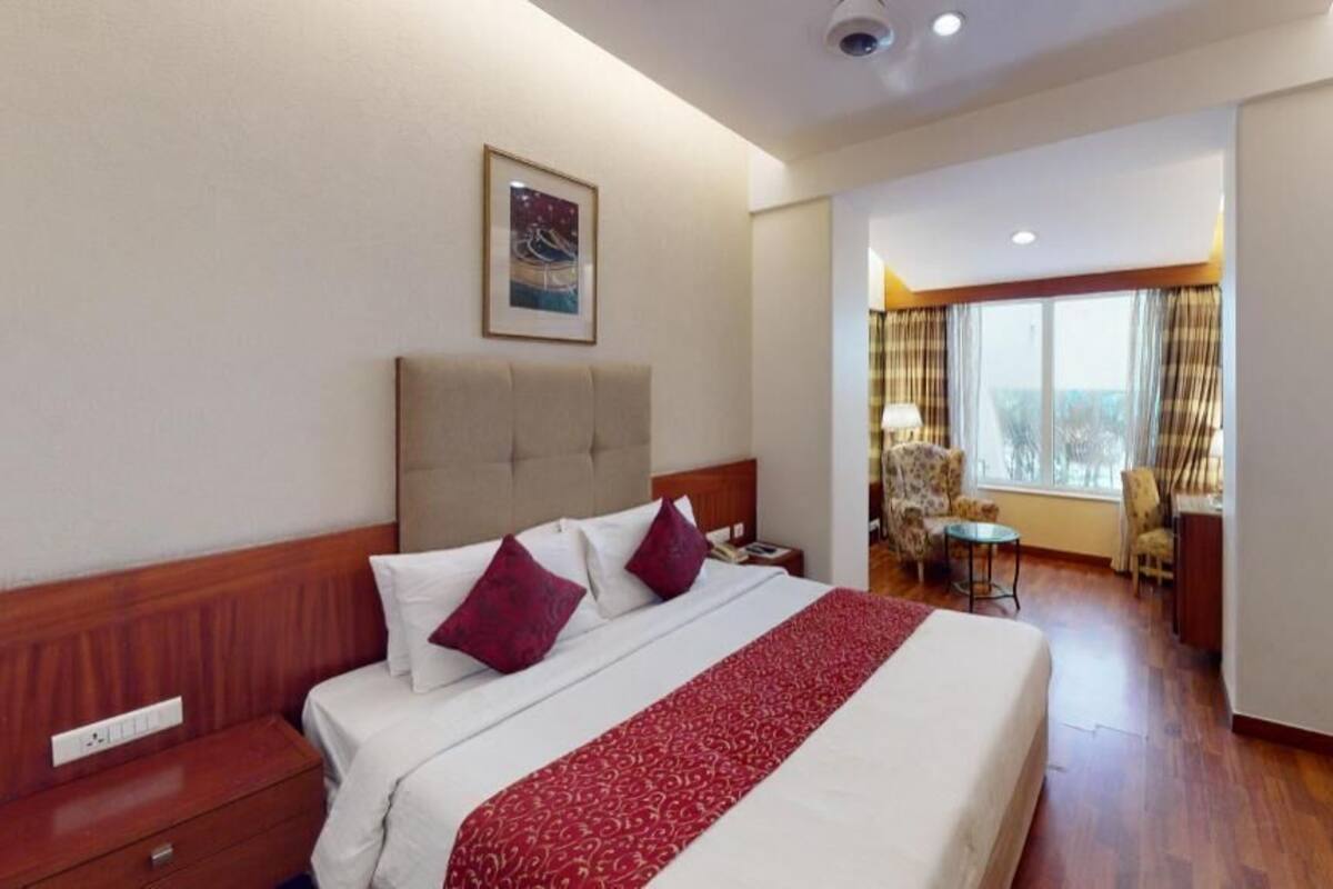 A hotel room with a bed, a desk, a chair, a TV, and a window with curtains.