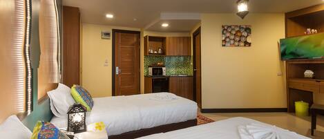 Habitación de hotel con dos camas, una kitchenette pequeña, un televisor y un adorno en la pared.