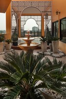 Un patio con una fuente, plantas en macetas y edificios al fondo.