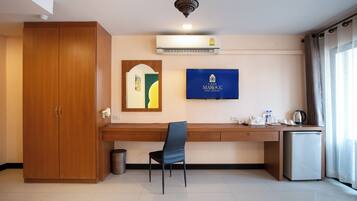 A hotel room with a wooden wardrobe, a desk with a chair, a television, and a mini fridge.