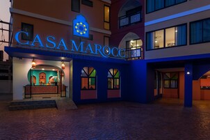 Exterior del hotel y resort Casa Maroc, con un llamativo letrero iluminado, una zona de recepción y un patio con suelo estampado.