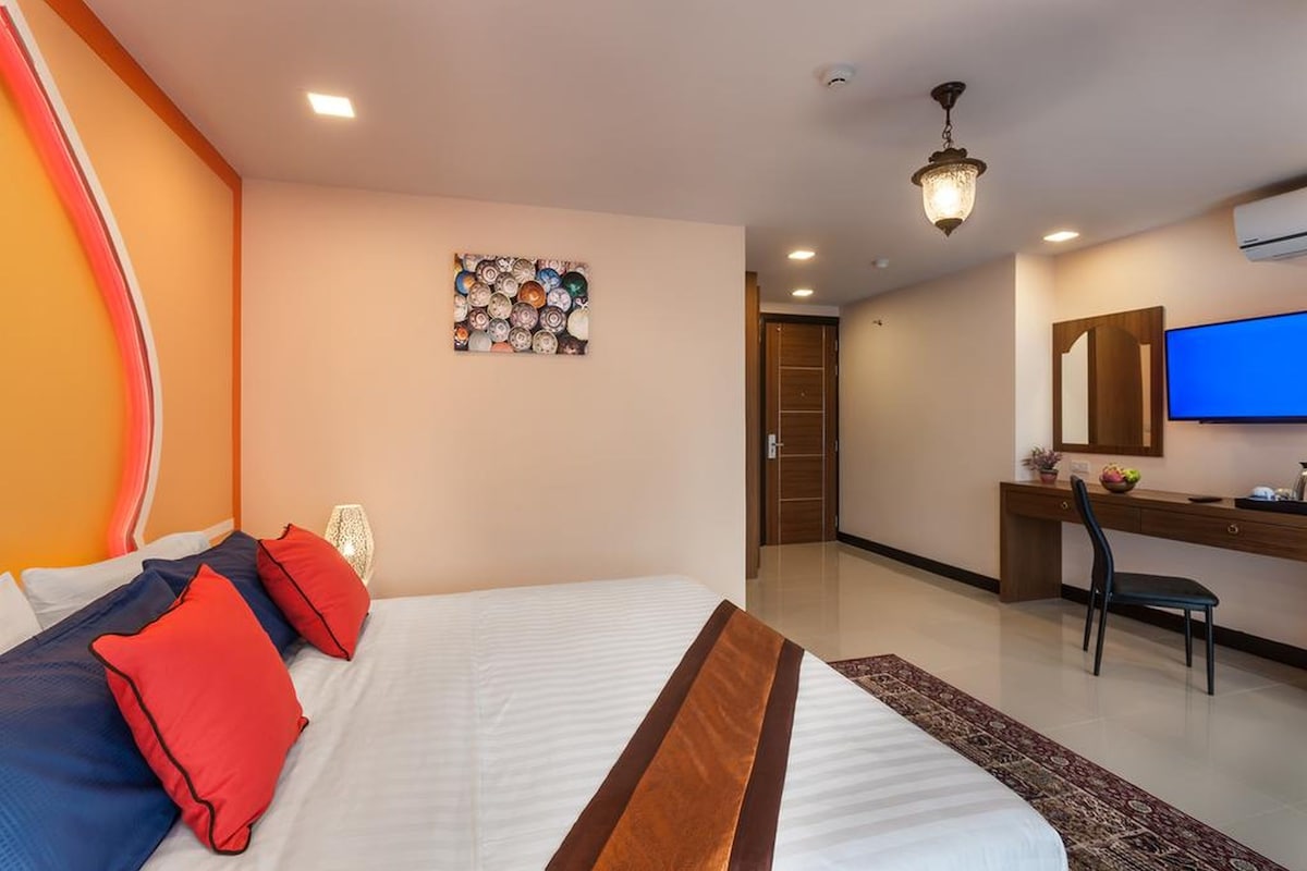 Una habitación de hotel con una cama, un escritorio, un televisor y una obra de arte en la pared.