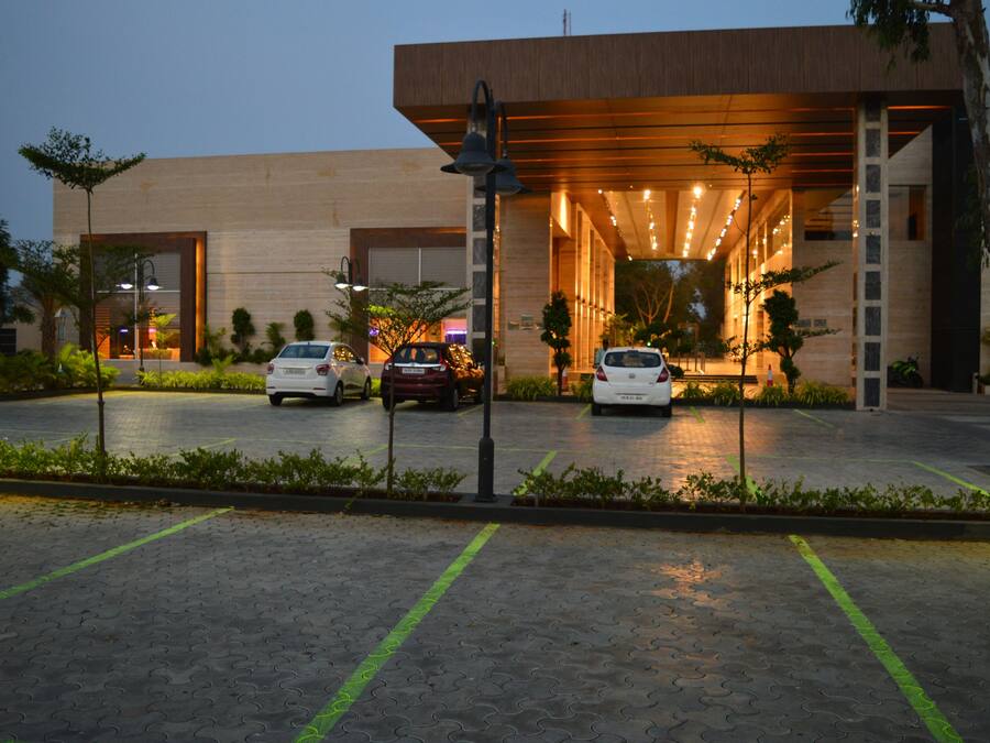A modern building with a covered entrance, a parking area with marked spaces, and a well-maintained garden.