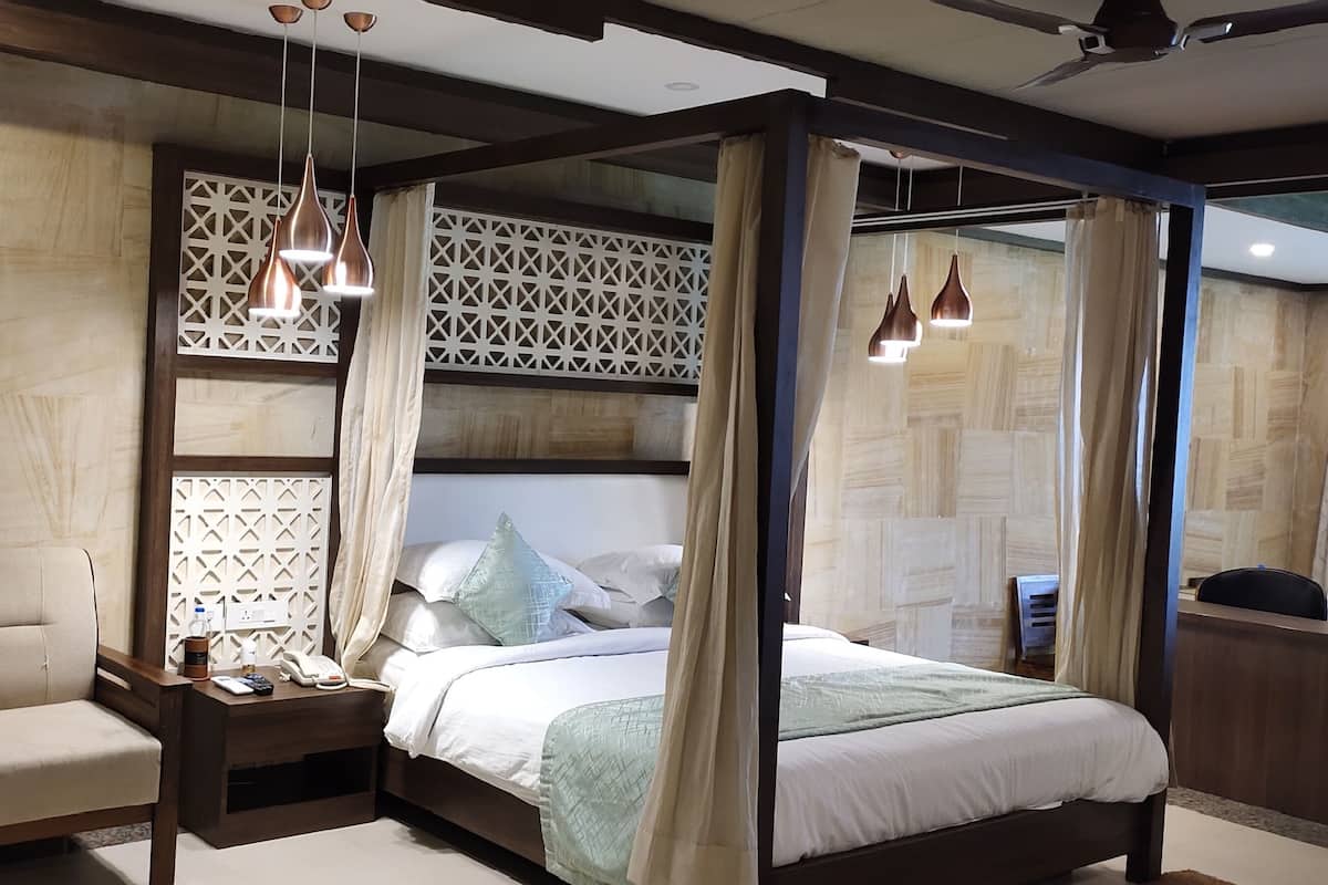 Una habitación de hotel moderna con una cama con dosel, una mesita de noche de madera, un área de descanso con dos sillones y un panel decorativo en la pared.