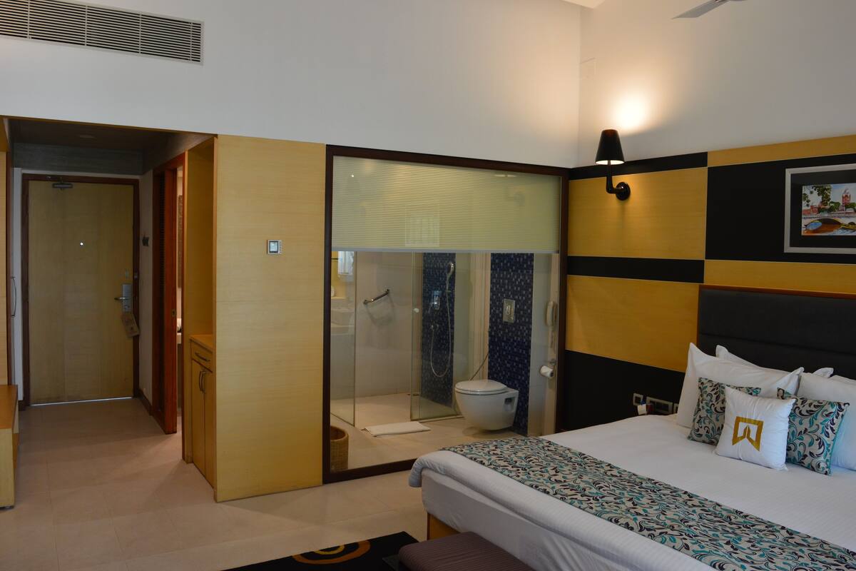 Una habitación de hotel con cama, baño con ducha y puerta que da a otra habitación.