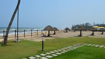 A beach with thatched-roof structures, a pathway, and a view of the ocean.