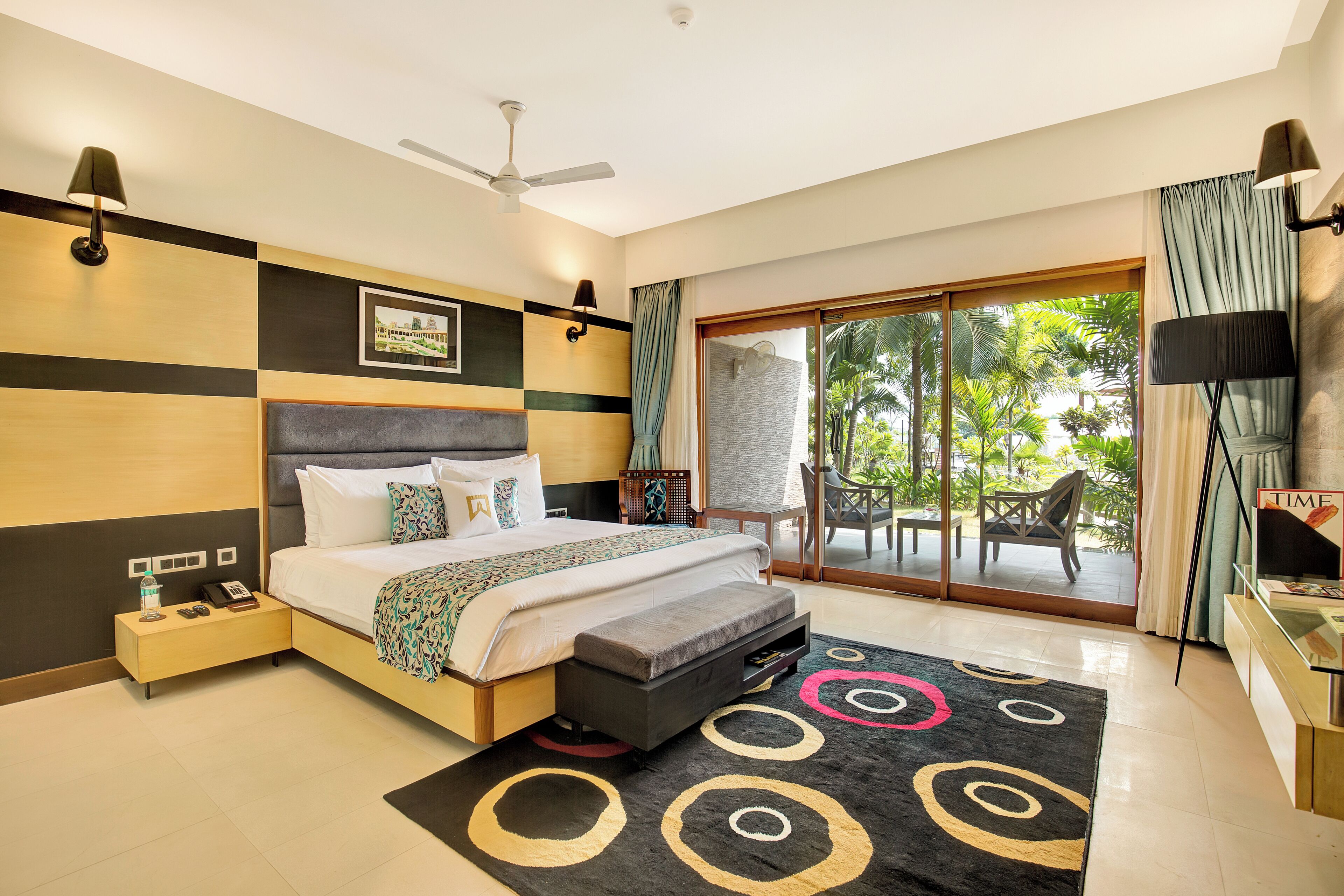 Habitación de hotel moderna con cama, mesita de noche, lámpara y vistas al exterior.
