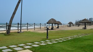 Une plage avec des parasols en chaume, une promenade bordée de barrières et des palmiers.