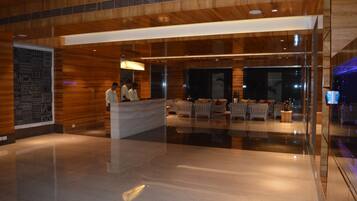 A modern hotel lobby with a reception desk, seating area, and large windows.