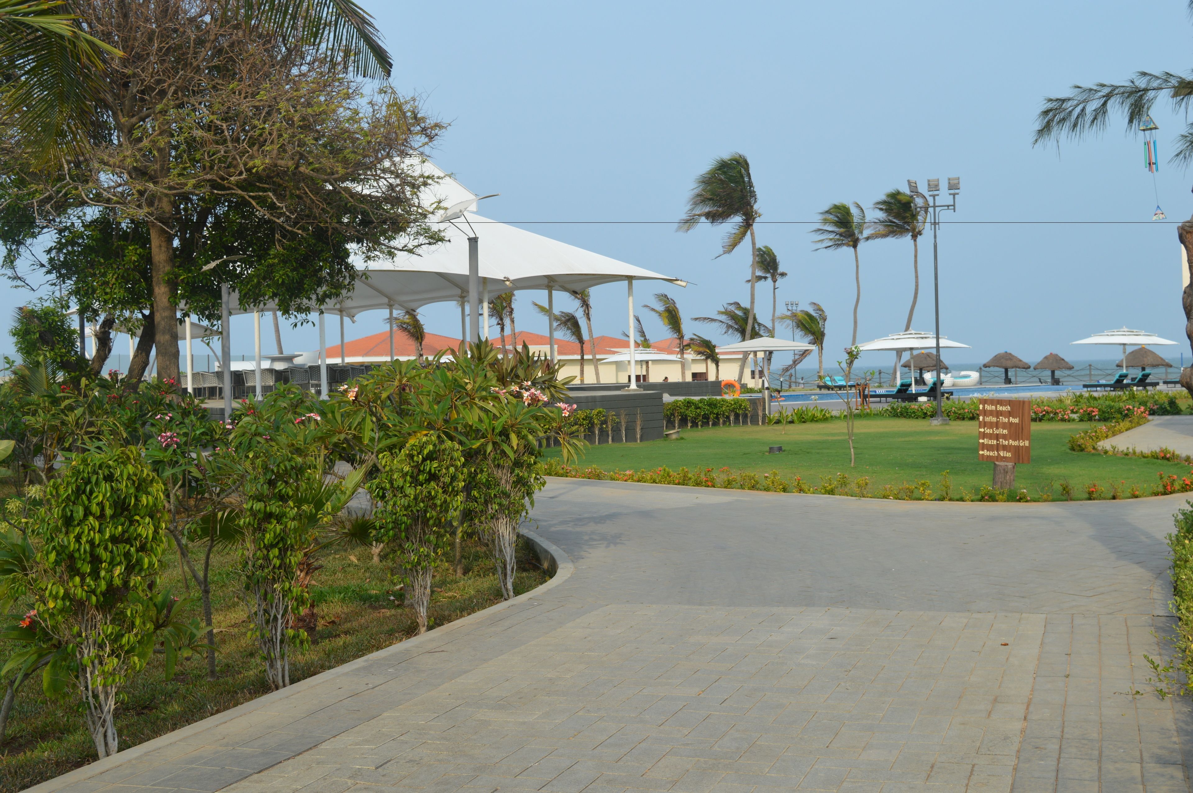 Un chemin pavé mène à une zone de plage aménagée avec des parasols et des chaises longues.
