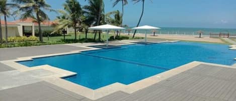 Una piscina con cubierta de madera, rodeada de palmeras y vista al océano.