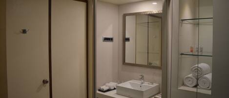 Un baño de hotel con un lavamanos blanco, un espejo grande y una cabina de ducha de vidrio.