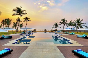 A resort pool area with lounge chairs and umbrellas, surrounded by palm trees. - Welcomhotel by ITC Hotels, Kences Palm Beach, Mamallapuram (Tirukalukundram)