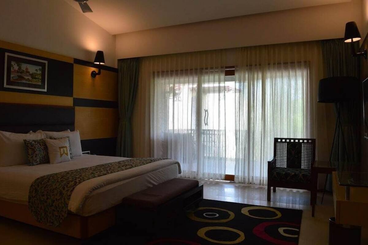 Una habitación de hotel con cama, una silla, un escritorio y ventana con cortinas.