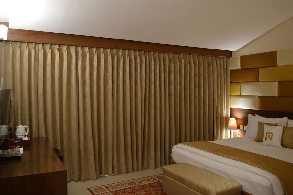 Habitación de hotel con una cama grande, un escritorio con computadora y una ventana con cortinas.