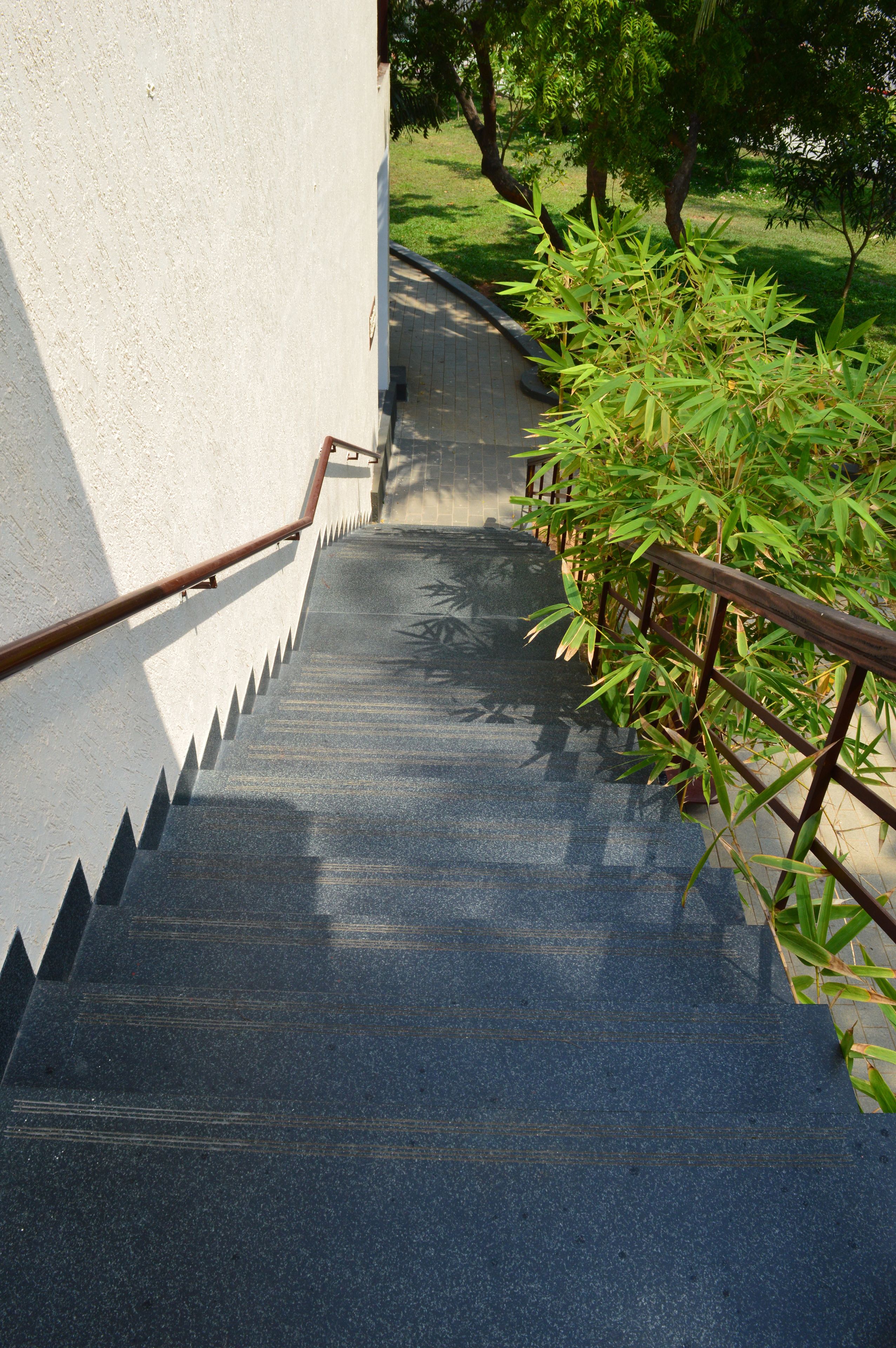 Un escalier en béton avec des rampes métalliques et un chemin pavé qui le longe.