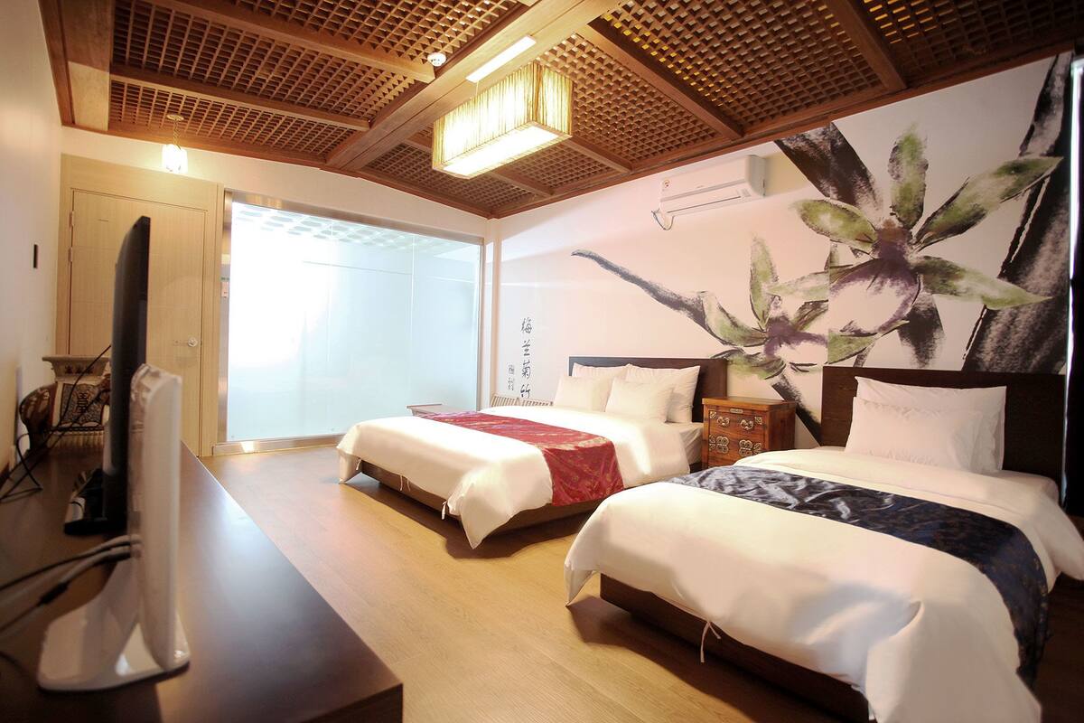 A hotel room with two beds, wooden flooring, a ceiling with a wooden lattice design, and a large wall painting.